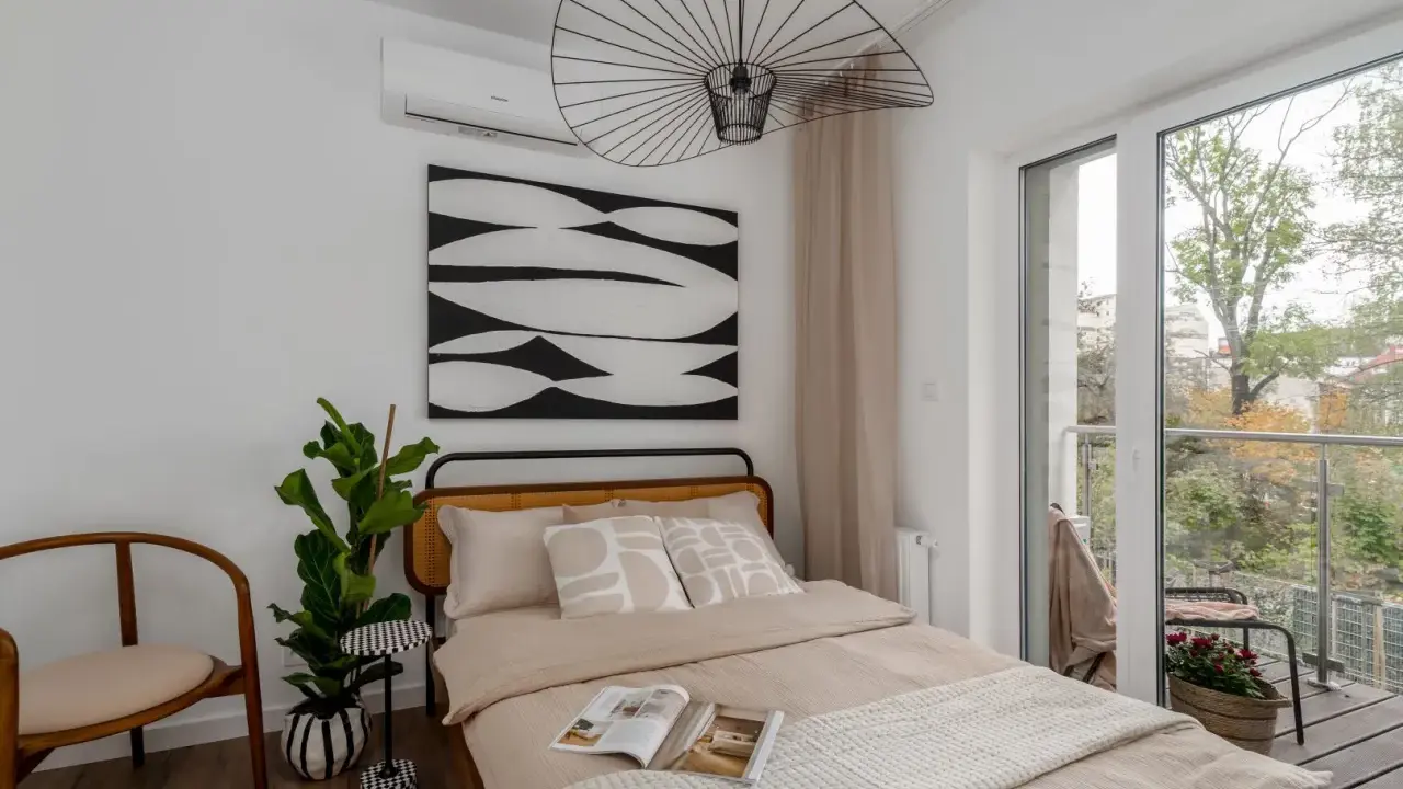 Przytulne lozko pod oknem z widokiem na balkon i zieleń. Wygodne poduszki i ciekawa grafika na ścianie tworzą relaksującą atmosferę.