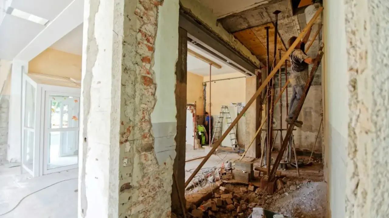 Remont mieszkania krok po kroku: pracownik na drabinie, gruz i materiały budowlane.