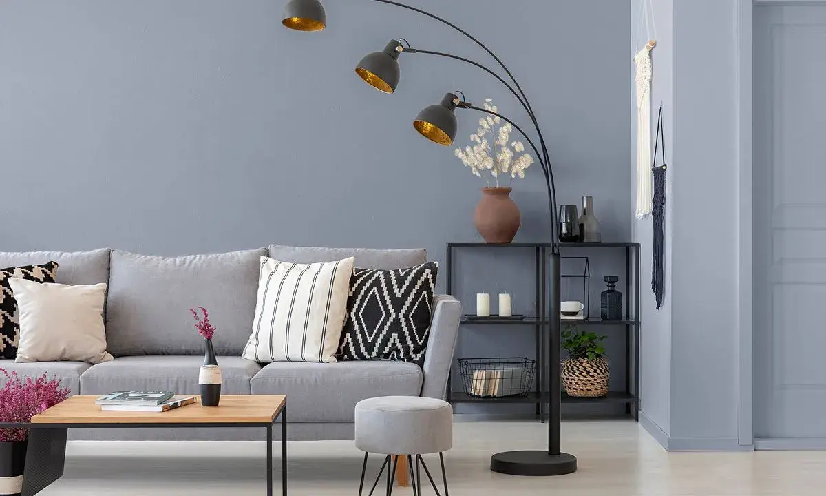 Sofa w kolorze grafitowym i szarym, ozdobiona poduszkami. Obok stolik kawowy i pufka.