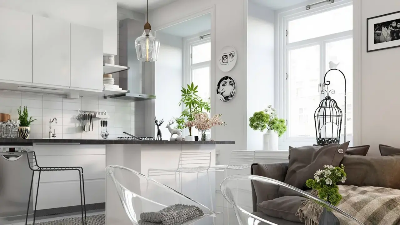Nowoczesny salon z aneksem kuchennym, jasne wnętrze z białymi meblami, przezroczystymi krzesłami i szarą kanapą.