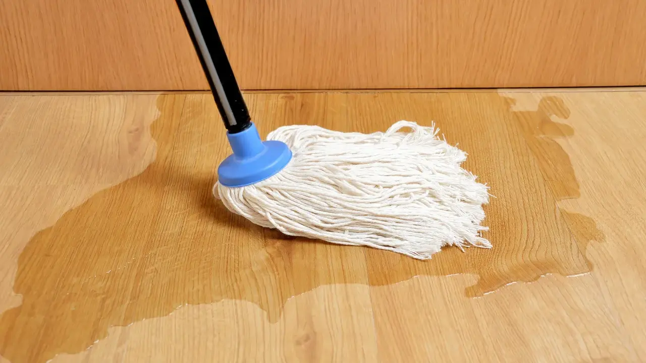 Mop na drewnianej podłodze, gdzie woda pod panelami tworzy kałuże.