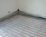Instalacja ogrzewania podłogowego pod przyszłymi meblami. Białe rurki ułożone na siatce izolacyjnej.