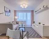 Jak umeblować pokój 4x5? Nowoczesny salon z szarą kanapą, stolikiem kawowym, dywanem i białym regałem.
