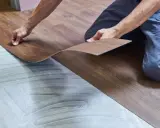 Ręce układają panel winylowy imitujący drewno na przygotowanym podłożu. Trwa wymiana panela winylowego.