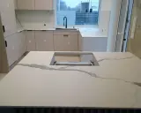 Nowoczesna kuchnia z wyspą i blatami z białego spieku kwarcowego, imitującego marmur.