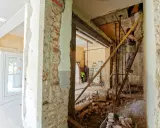 Remont mieszkania krok po kroku: pracownik na drabinie, gruz i materiały budowlane.