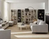 Nowoczesny salon beżowo szary z szarą kanapą, białymi regałami i czarną szafką.