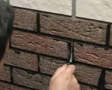 Ręka wygładza fugę między cegłami klinkierowymi. Prace wykończeniowe przy elewacji.