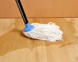 Mop na drewnianej podłodze, gdzie woda pod panelami tworzy kałuże.