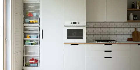 Nowoczesna kuchnia z otwartą lodówką pełną świeżych warzyw i owoców. Białe meble, piekarnik i płyta gazowa to stylowe agd do kuchni.