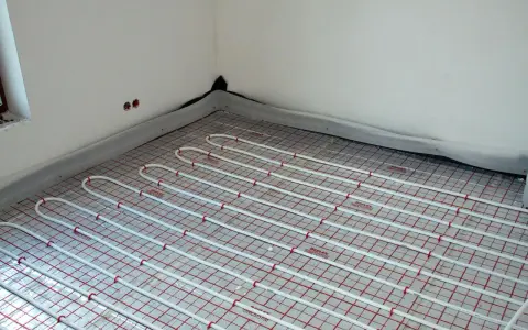 Instalacja ogrzewania podłogowego pod przyszłymi meblami. Białe rurki ułożone na siatce izolacyjnej.