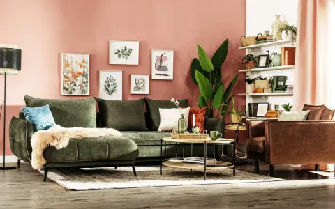 Przytulny salon z zieloną kanapą i brązowym fotelem. Ściany w kolorze pudrowego różu, ozdobione obrazami.