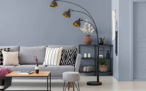 Sofa w kolorze grafitowym i szarym, ozdobiona poduszkami. Obok stolik kawowy i pufka.