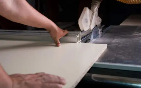 Precyzyjne cięcie blatu laminowanego na pile tarczowej. Ręka prowadzi materiał, zapewniając idealną linię cięcia.