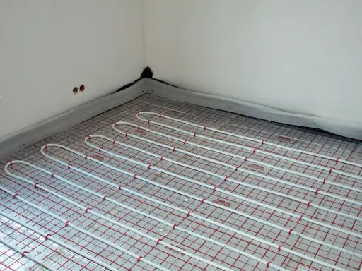 Instalacja ogrzewania podłogowego pod przyszłymi meblami. Białe rurki ułożone na siatce izolacyjnej.