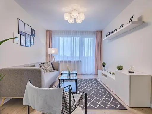 Jak umeblować pokój 4x5? Nowoczesny salon z szarą kanapą, stolikiem kawowym, dywanem i białym regałem.
