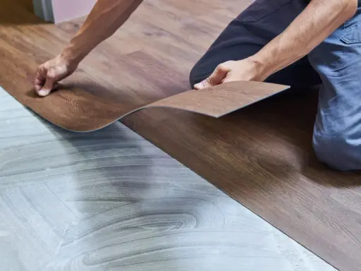 Ręce układają panel winylowy imitujący drewno na przygotowanym podłożu. Trwa wymiana panela winylowego.