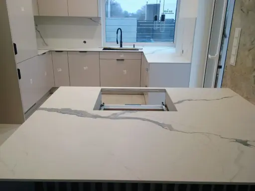 Nowoczesna kuchnia z wyspą i blatami z białego spieku kwarcowego, imitującego marmur.