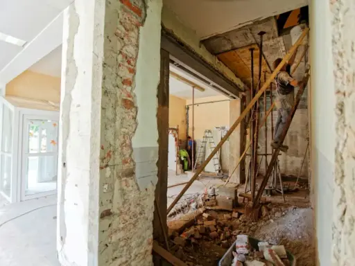 Remont mieszkania krok po kroku: pracownik na drabinie, gruz i materiały budowlane.