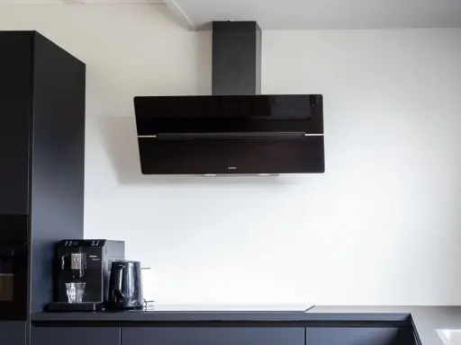 Nowoczesna kuchnia z czarnymi szafkami. Okap nad płytą indukcyjną zamontowany na odpowiedniej wysokości, by zapewnić komfort gotowania.