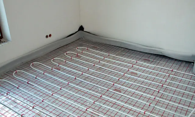 Instalacja ogrzewania podłogowego pod przyszłymi meblami. Białe rurki ułożone na siatce izolacyjnej.