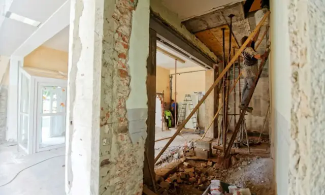 Remont mieszkania krok po kroku: pracownik na drabinie, gruz i materiały budowlane.