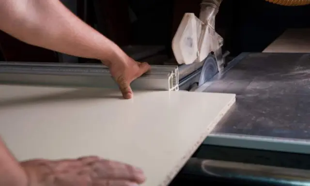 Precyzyjne cięcie blatu laminowanego na pile tarczowej. Ręka prowadzi materiał, zapewniając idealną linię cięcia.
