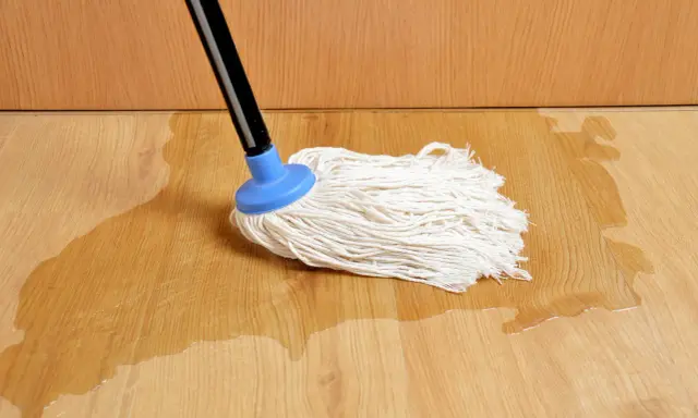 Mop na drewnianej podłodze, gdzie woda pod panelami tworzy kałuże.