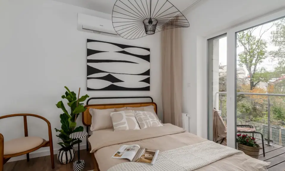 Przytulne lozko pod oknem z widokiem na balkon i zieleń. Wygodne poduszki i ciekawa grafika na ścianie tworzą relaksującą atmosferę.