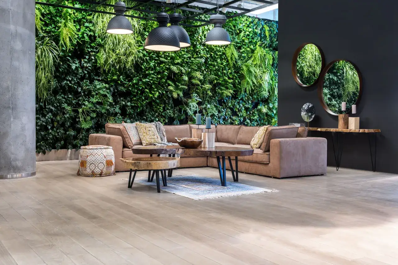 Brązowa sofa i beżowe poduszki świetnie komponują się z zieloną ścianą roślin. Jaki kolor pasuje do brązu i beżu? Zieleń natury!