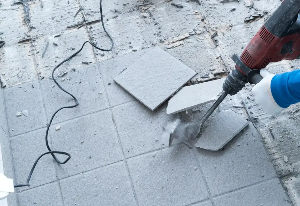 Młotowiertarka rozbija płytki, pokazując, jak skuć płytki bez kurzu.
