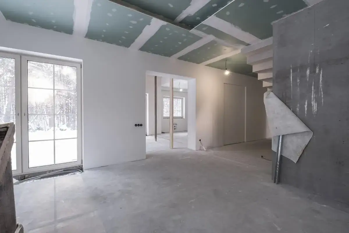 Wnętrze w trakcie prac wykończeniowych. Widoczne sufity podwieszane, ściany z gładzią, betonowa posadzka i schody. To etap wykończenie mieszkania krok po kroku.